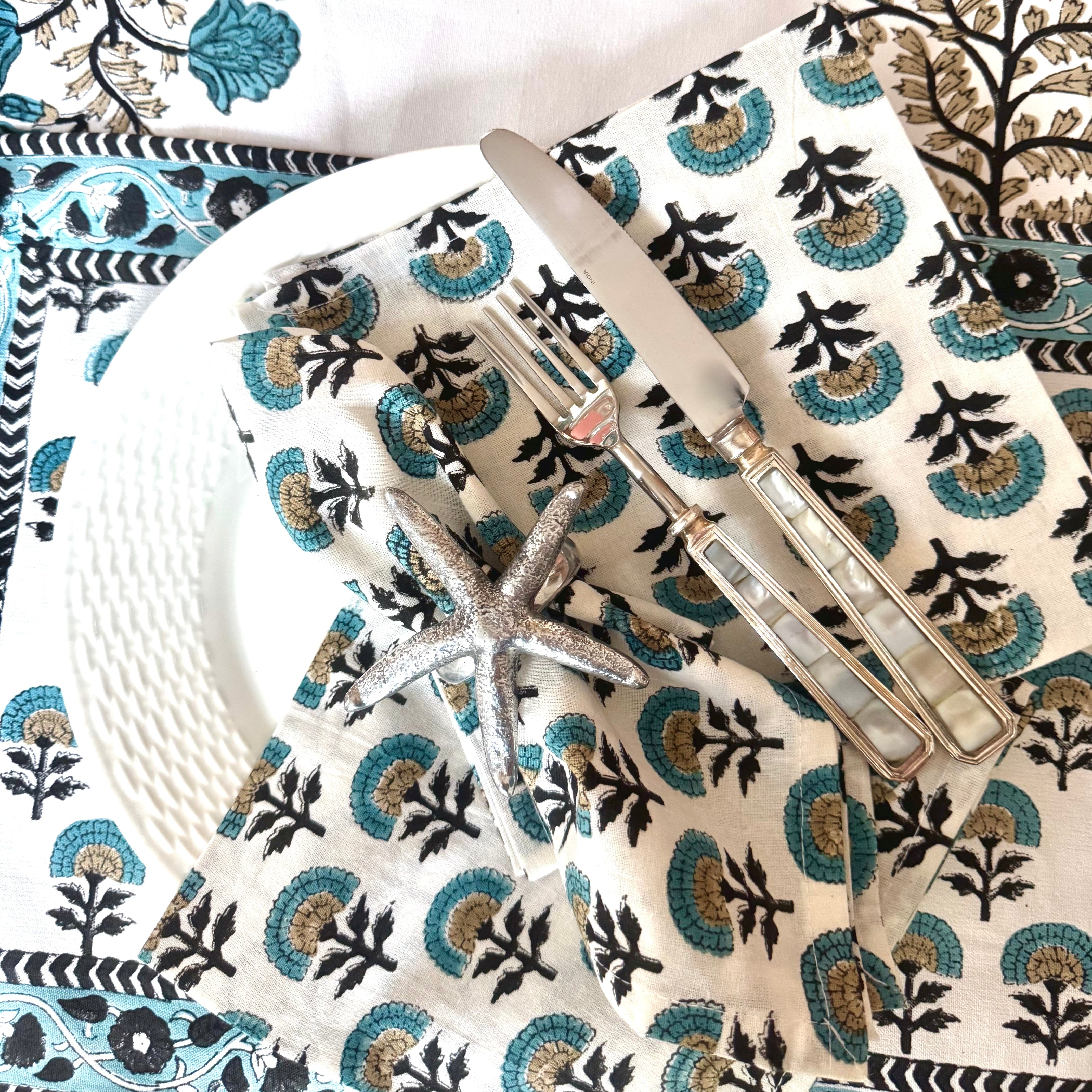 Table setting with floral placemats, napkins, and table runner, white plates, and silver cutlery.