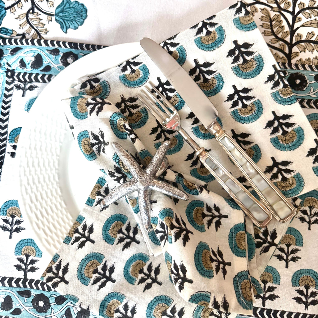 Table setting with floral placemats, napkins, and table runner, white plates, and silver cutlery.