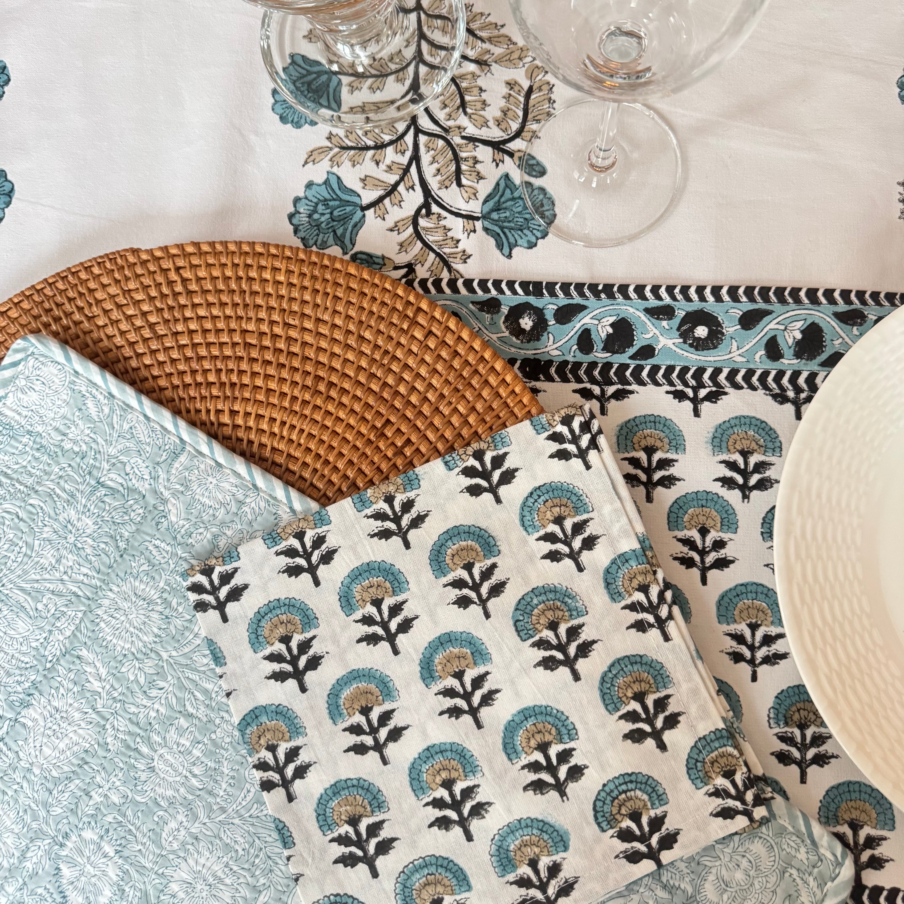 Table setting with floral-patterned table runner, placemats, napkins, white plates, and glasses.