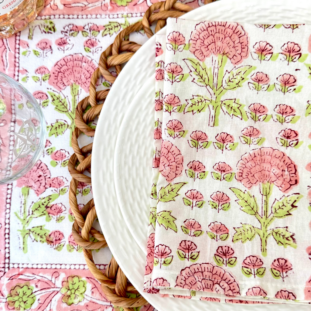 Floral-patterned napkin on a matching placemat with a woven placemat underneath with two white plates a glass and a bottle of wine.
