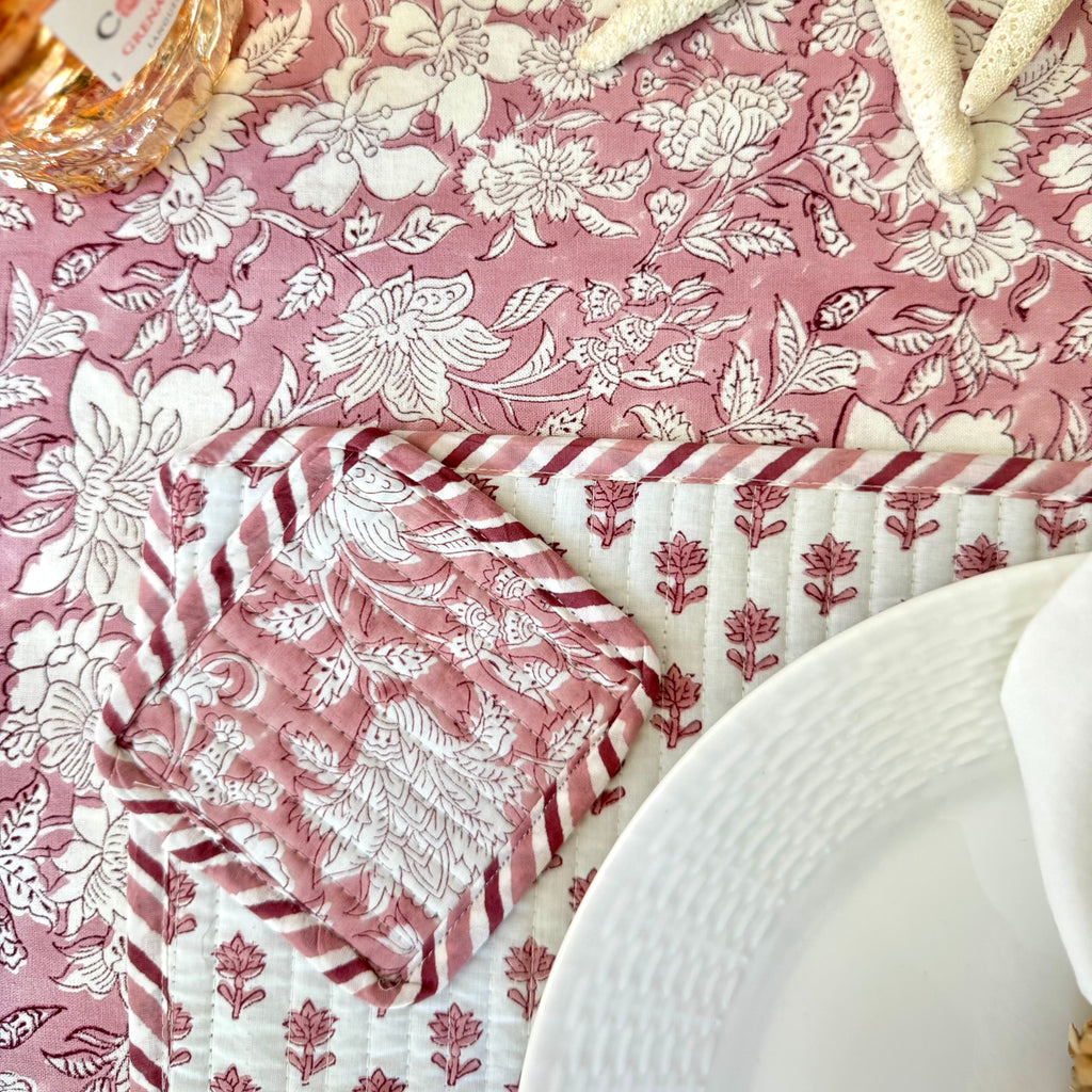 Table setting with floral tablecloth coaster, and placemat, white plate, white napkin with woven napkin ring, starfish decoration, and bottle of wine.