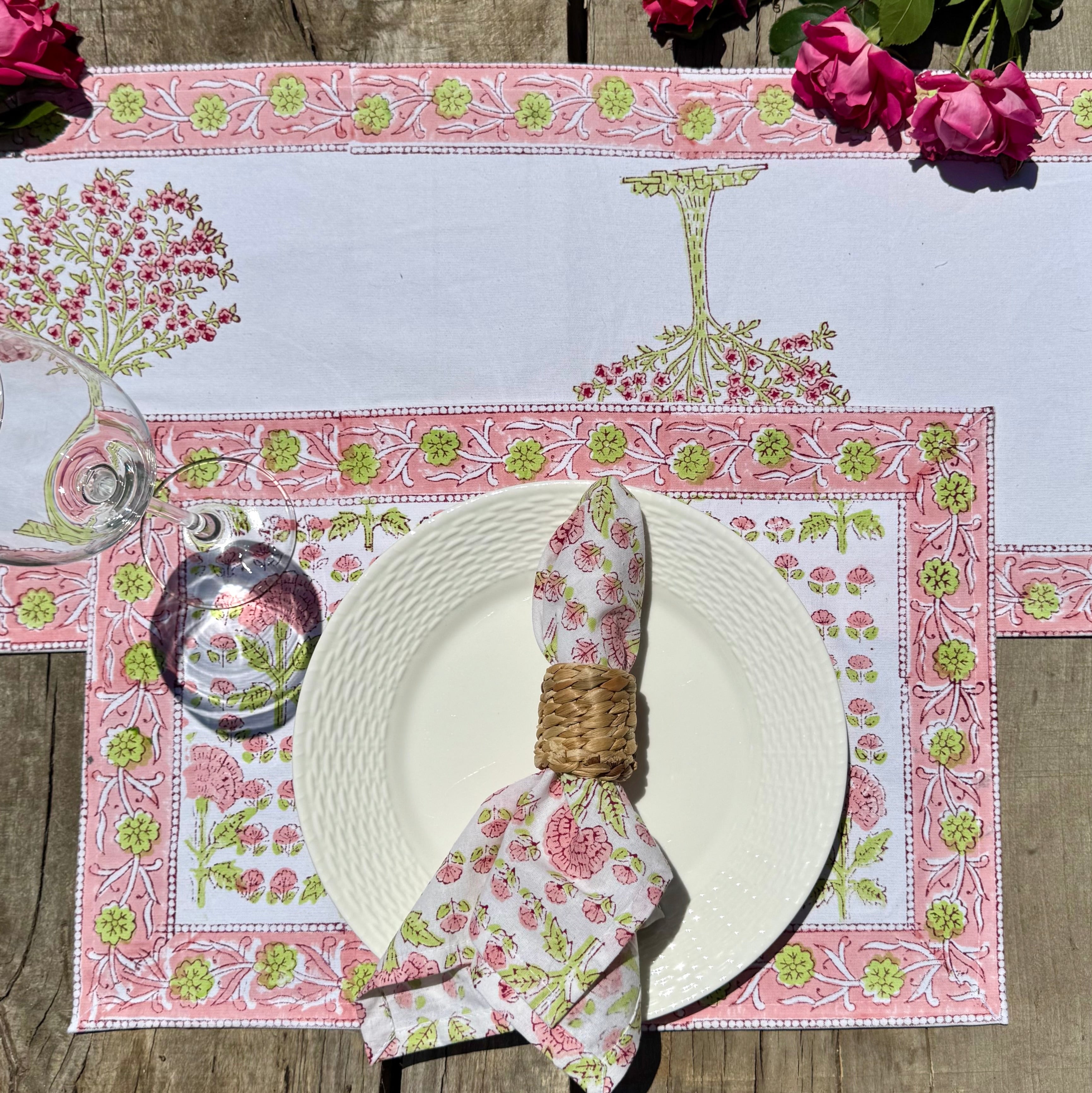 Decorative table setting with a pink floral placemat, white plate, and floral napkin on a wooden surface.