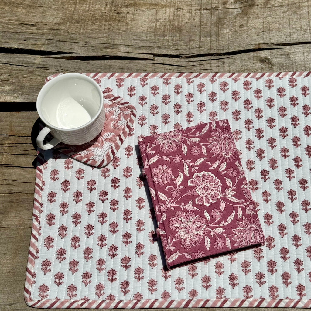 Floral-patterned placemat with a cup and floral patterned notebook and coaster with mug on a wooden surface