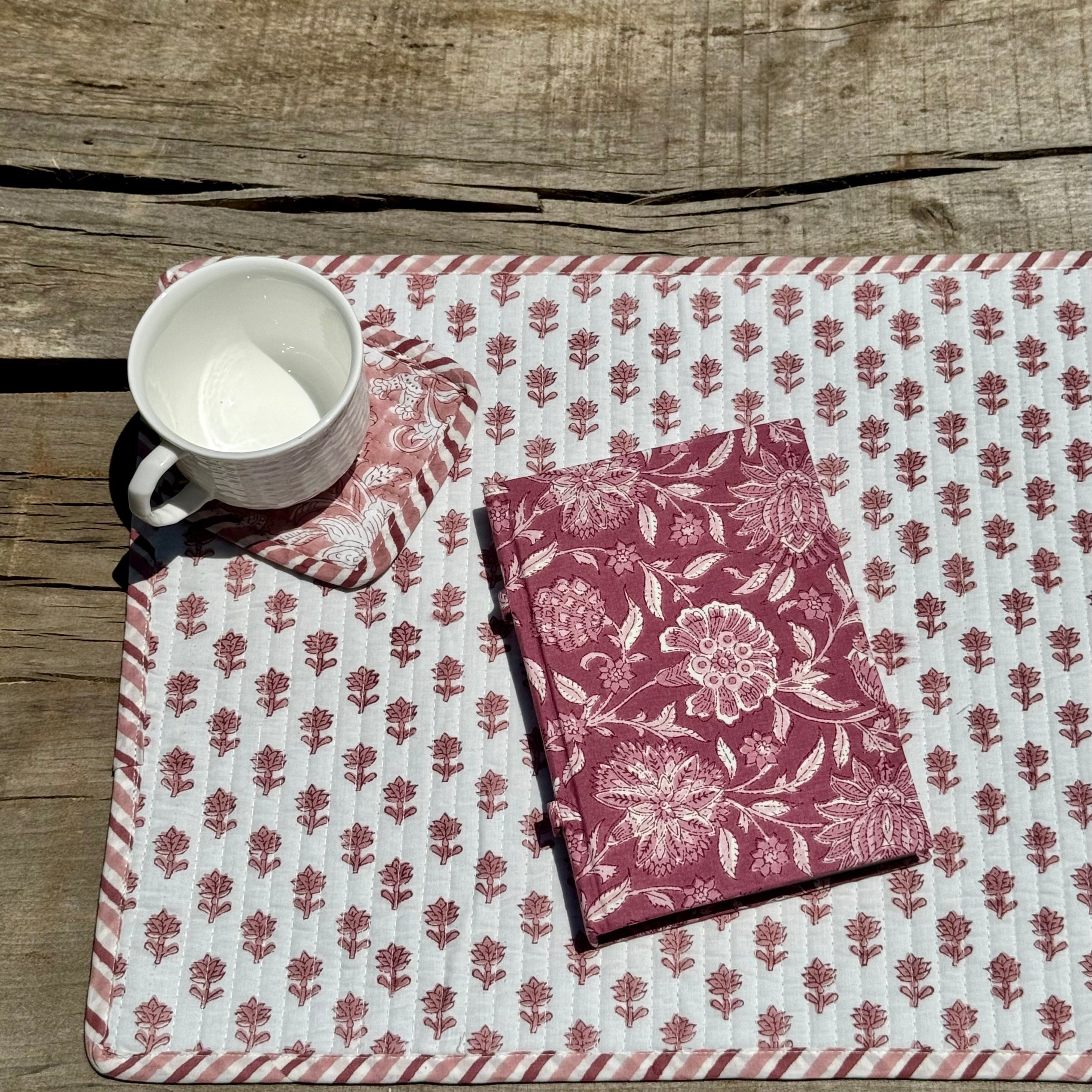 Floral-patterned placemat with a cup and floral patterned notebook and coaster with mug on a wooden surface