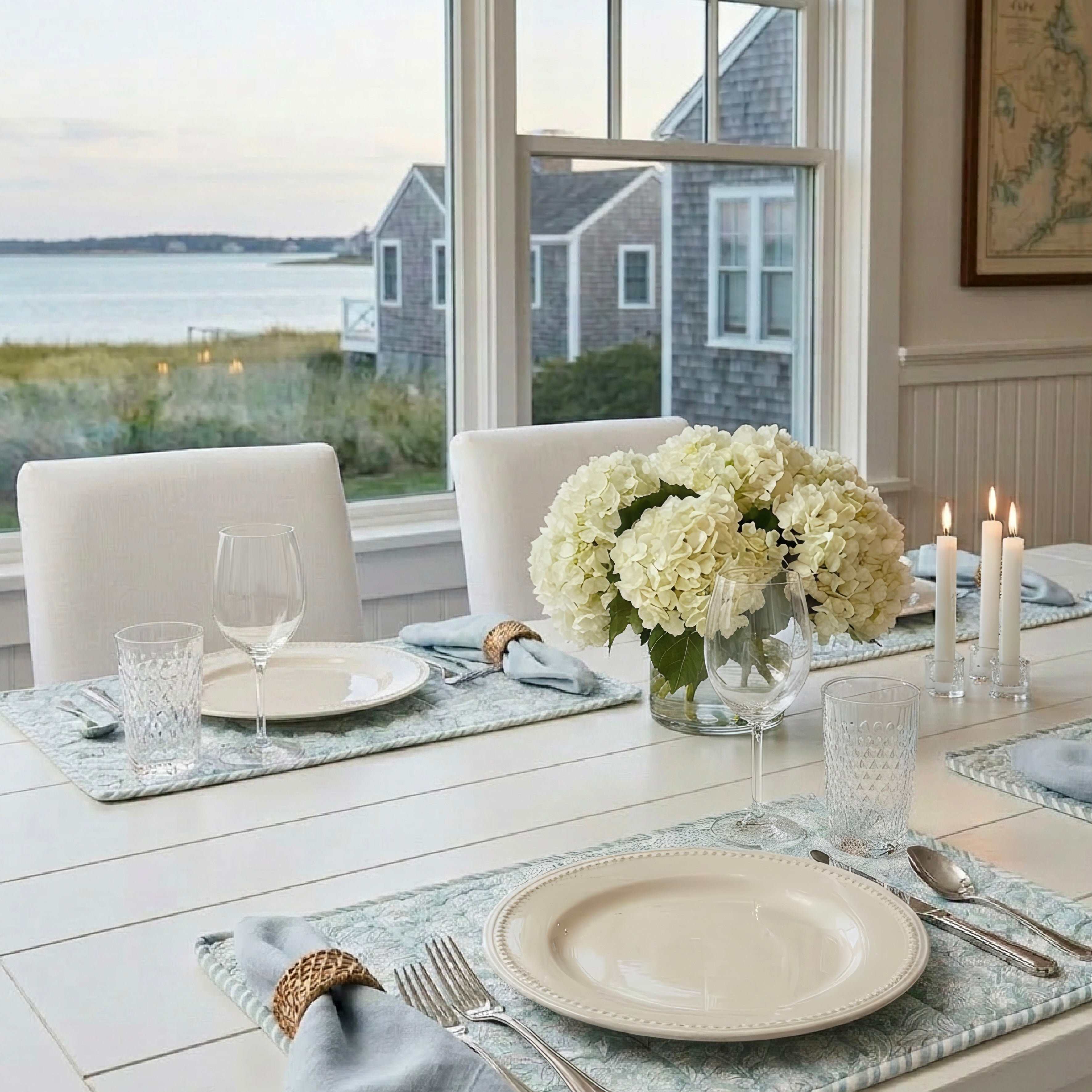 Dining room table set for a meal with white flowers, candles, and views of houses and water.
